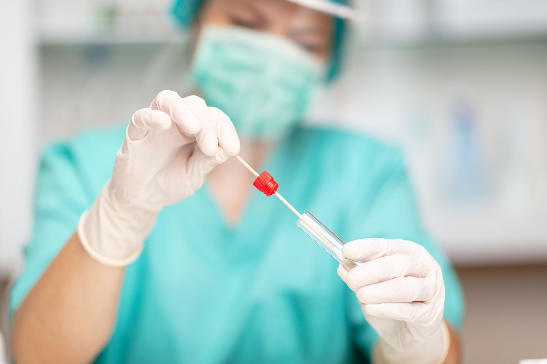 Healthcare worker in protective workwear putting swab stick into test tube